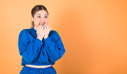 Nervous woman biting her fingernails. Anxiety problems. Orange background. 20-22 years old woman. Caucasian woman.