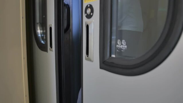 a woman passenger passes from one train car to another car by pressing the button of an electric sliding door. The door will close automatically