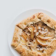Close up on French galette with pears filling, allspice, honey and almond sprinkle. Homemade rustic pie. Easy and simple baking recipes. Home cooking from scratch lifestyle. Food flat lay, top view.