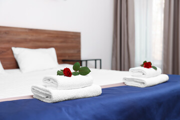 Clean folded towels with flowers on bed in hotel room