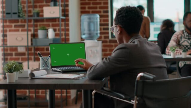 Man with disability looking at greenscreen on computer, sitting in wheelchair. Office worker using isolated template with blank chromakey and copyspace background on laptop display.