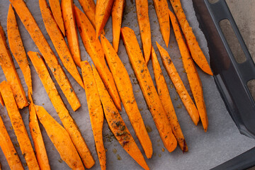 Sliced raw orange sweet potato wedges with spices and oil on parchment paper on a baking sheet
