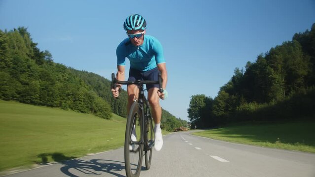 Professional road cycling male racer taking an aerodynamic body position for sprinting on a bike, front view.