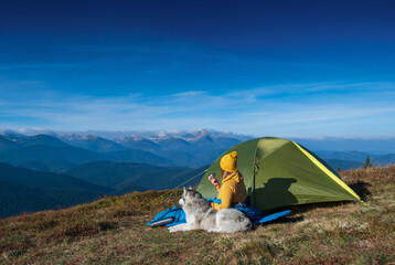 A young girl with Siberian husky dog near the tent with mountains peaks on background © Taras