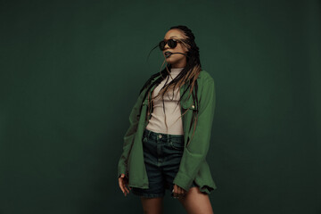 Monochrome portrait of female fashion model in shorts and shirt isolated on dark green background....