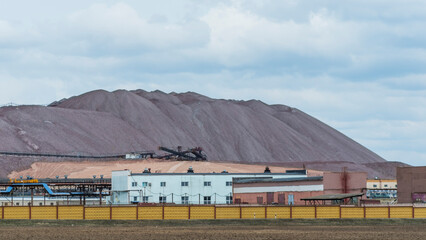 Mountains of empty ore when mining potassium on cloudy sky background. Transportation of an empty rock to a dump.