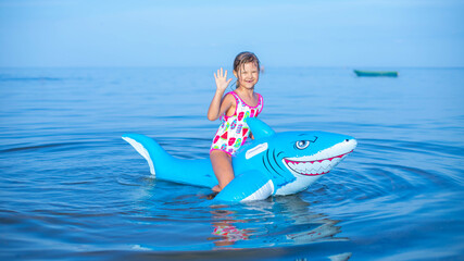  Happy girl swimming on an inflatable shark toy in the sea