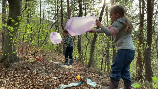 Preschool kids holding garbage bags, preparing to collect plastic outdoors. Little girl and boy blowing plastic bags with wind in forest. Young volunteers ready to save nature in any weather condition