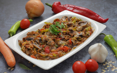 Mushroom sauteed with peppers and tomatoes, onions, garlic and olive oil on a white plate, on wooden background.