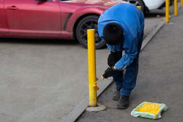 Fototapeta premium Painting a metal post with yellow paint. Parking bollard painting.