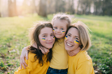 Fototapeta na wymiar Portrait of Ukrainian family. Mom with two little daughters hugging and smiling in nature on sunny day.
