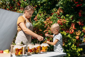 Happy family mother and son kid canning vegetables in the garden in summer day. Canning and Preserve Vegetables From Garden