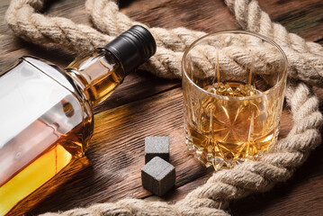 Fototapeta premium Whiskey in the drinking glass, bottle and mooring rope on the brown wooden table background.
