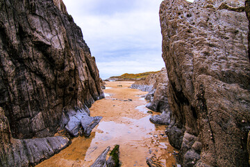 A sandy channel, revealed by low tide, leads through the rocks towards the sea and headland in the distance.