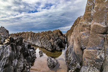 A beautiful clear rock pool, surrounded by dramatic rocks, with a stormy sky.  Mortehoe, near Woolacombe in North Devon.