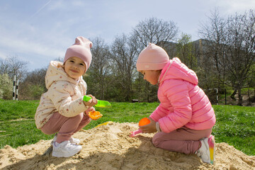 Adorable little girls have fun on the playground in the sandbox. Children play with sand molds and make Easter cakes. Creative outdoor activities for children. Girls in the sandbox outside