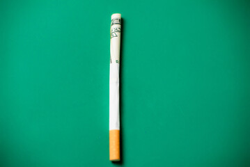 Smoking and money. Rolled up dollar bill in a cigarette. Green background. The high cost of smoking cigarettes concept.