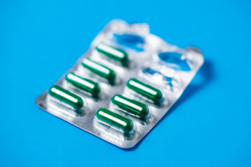Started packing of tablets with green capsules. Blue background background. Probiotics, vitamins concept.