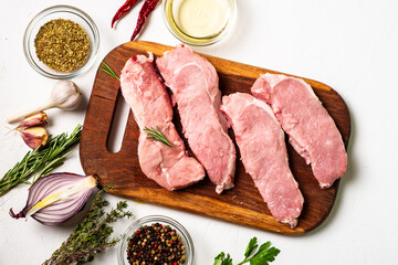 Raw meat steaks on a cutting board. White background. Preparation for cooking pork meat. Various spices, seasonings lie nearby.
