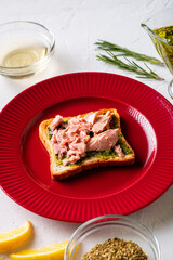 Toast with tuna and chimichurri sauce on a red plate. White background.