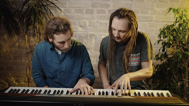 Music lesson. Young man with dreadlock studying to play on digital piano, male teacher showing keys, tracking shot
