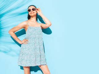Young beautiful smiling female in trendy summer dress. Sexy carefree woman posing near blue wall in studio. Positive brunette model having fun.Cheerful and happy. Isolated