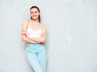 Young beautiful smiling female in trendy summer jeans and top. Sexy carefree woman posing near grey wall in studio. Positive brunette model having fun and going crazy. Cheerful and happy