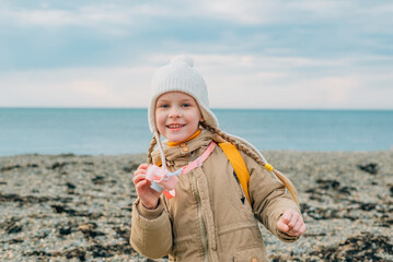 little cheerful girl with a smile shows the screen of a childrens pink camera in autumn on the sea. the child rejoices at the pictures taken of the autumn, spring seascape