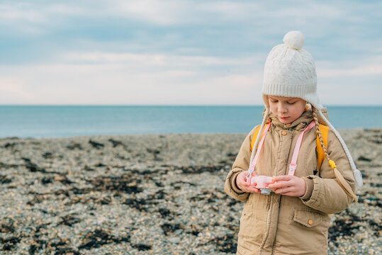 little girl looks at the screen of a children's pink camera to see her photos of the autumn, spring seascape. the child is passionate about his hobby: photography