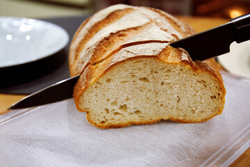 Sharp black knife cut the fresh bread on the table. Kitchen background and still life