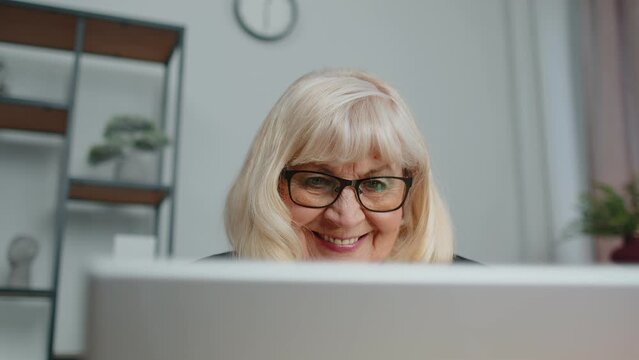 Senior mature older business woman wears glasses remote working, social distance elearning, training, online webinar at home office, using laptop computer. Close-up face elderly grandmother freelancer