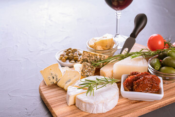 Charcuterie board with cheese slices and assortment of traditional Italian antipasti, cheese plate and glass of red wine on dark concrete background with copy space