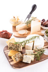 Wooden cheese board with selection of cheeses served together with olives and sun-dried tomatoes on white table. Cheese plate with craft cheeses for aperitif. Vertical image