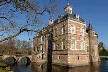 Obraz premium Stone bridge access to moated brick exterior facade of the Ruurlo castle picturesque painterly museum brightly lit seen trough winter barren branches