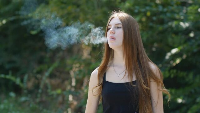 Portrait of a young girl smoking a vape. IQOS. Woman puffs on a vape pen. Blowing smoke out of your mouth is delicious.