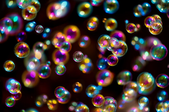 Gliding colorful bubbles isolated on black background with reflections. Soap bubbles are an extremely thin film enclosing air that forms a hollow sphere with an iridescent surface, partially blurred.