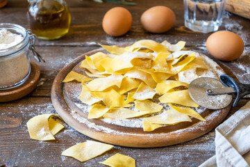 Homemade pasta Maltagliati on cutting board with ingredients on wooden background. Close up