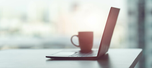 A dark laptop on the table with a coffee mug. in the office at home work at home concept