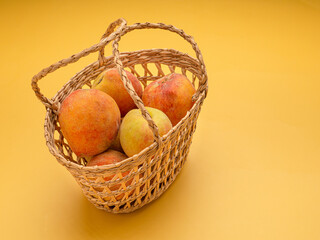 Group of fresh peaches fruits in a basket over a yellow background