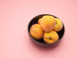 Fresh peaches fruit on a bowl over a pink background
