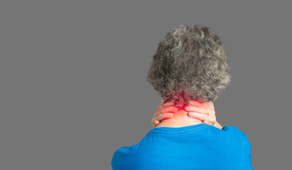 Back view of a senior woman suffering neck pain and neck tilt while standing against a gray...