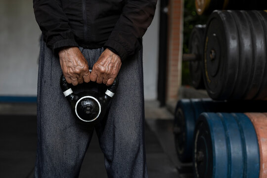 Unrecognizable Latin American senior male holding a kettlebell with both hands during his rehabilitation and therapy workouts at the gym. Healthy lifestyle concept.