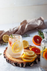 A glass and a decanter of lemonade. Lemon and grapefruit slices with rosemary leaves in a drink