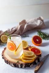 A glass and a decanter of lemonade. Lemon and grapefruit slices with rosemary leaves in a drink