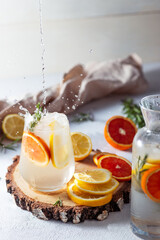 A glass and a decanter of lemonade. Lemon and grapefruit slices with rosemary leaves in a drink