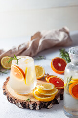 A glass and a decanter of lemonade. Lemon and grapefruit slices with rosemary leaves in a drink