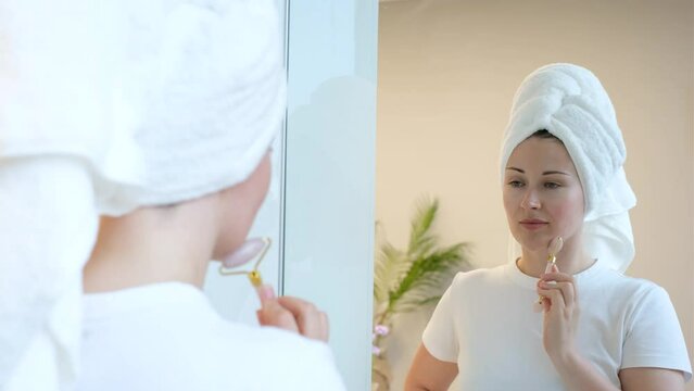 Young woman in white towel gives herself a massage with a jade roller.