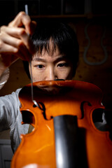 young chinese woman violin maker checking the quality of her violin