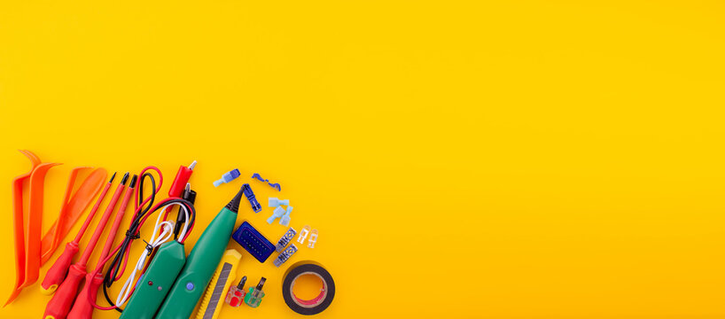 Arrangement of tools for repairing automotive electrical wiring on a yellow background.