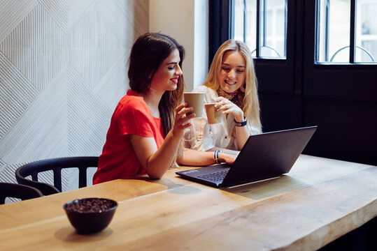 Cheerful friends using laptop in cafe